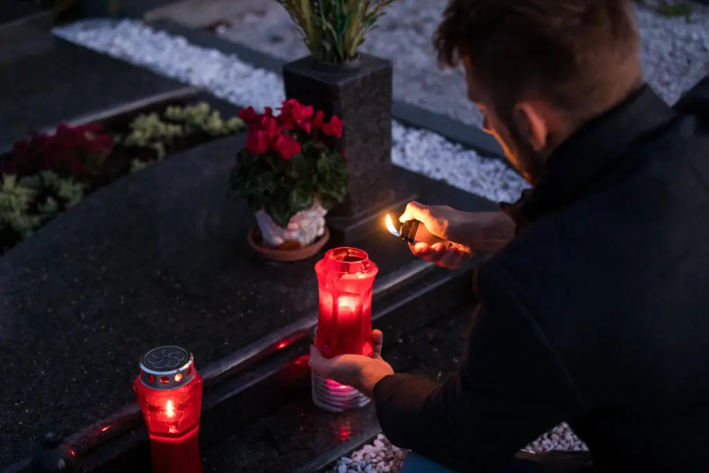 personne qui allume un cierge sur une pierre tombale